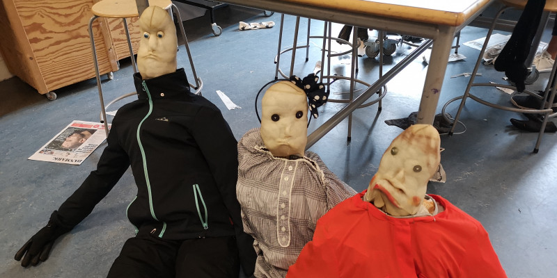 Dukker lavet af strømpebukser og glemt tøj sidder på gulvet i et klasseværelse.